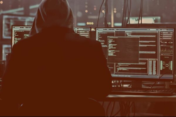 Cyber Security specialist in front of a PC with multiple monitors, displaying code-lines